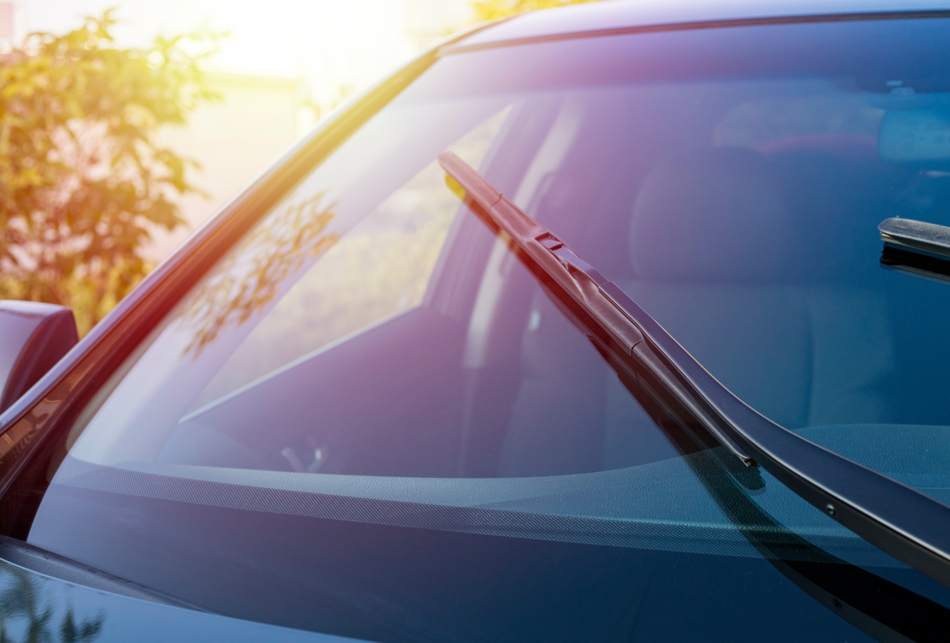 Windshield wipers clearing a car's windshield against a bright, sunny background.