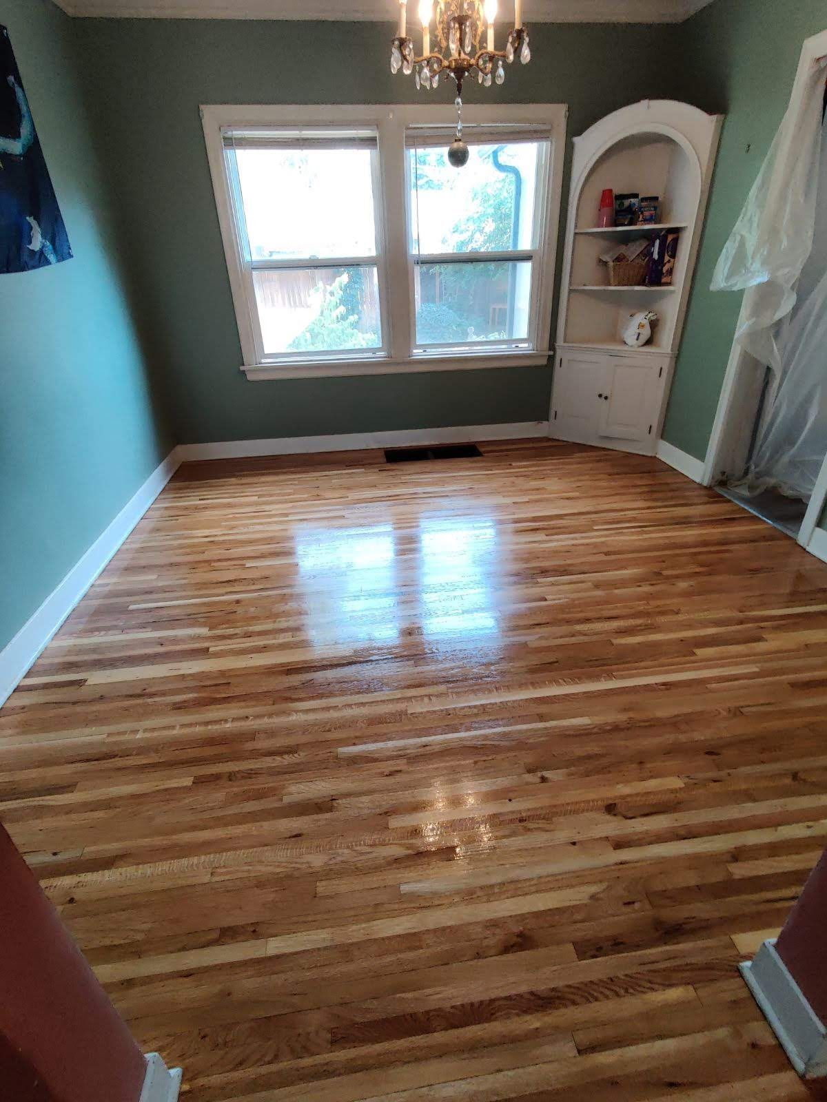 Newly refinished hardwood floor in a room with green walls, a window, and a built-in bookcase.
