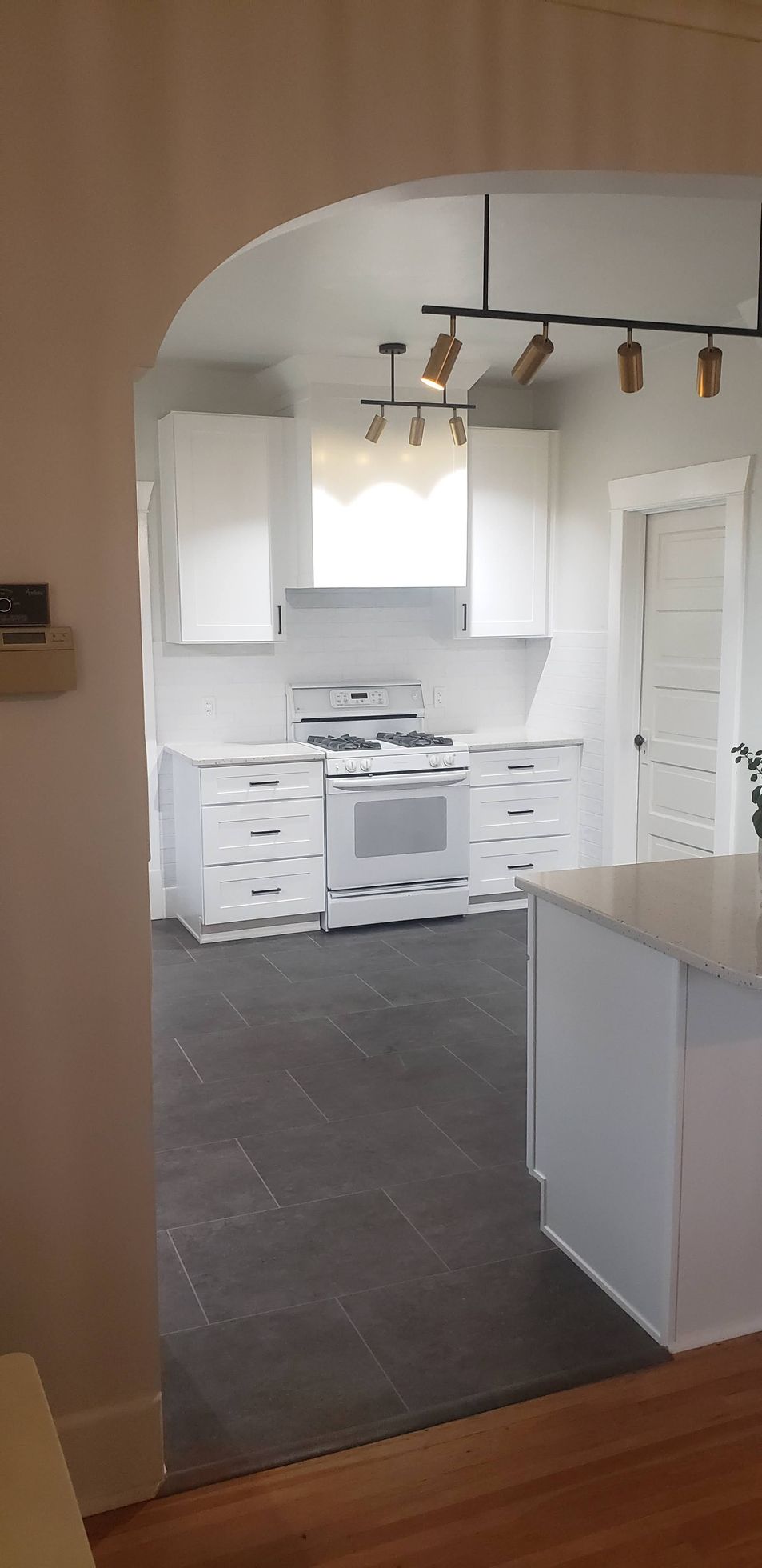 Kitchen with white cabinets, appliances, and dark gray tile flooring seen through an archway.