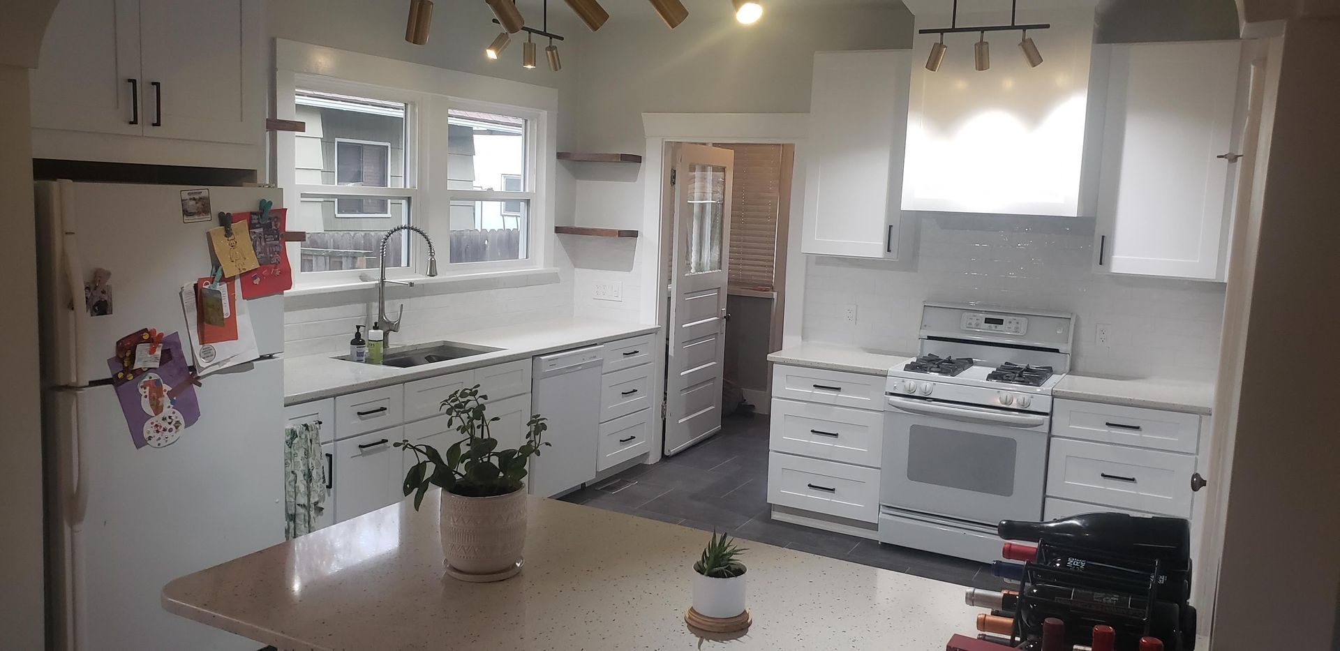 White kitchen with cabinets, stove, sink, and island; a house plant is on the island.