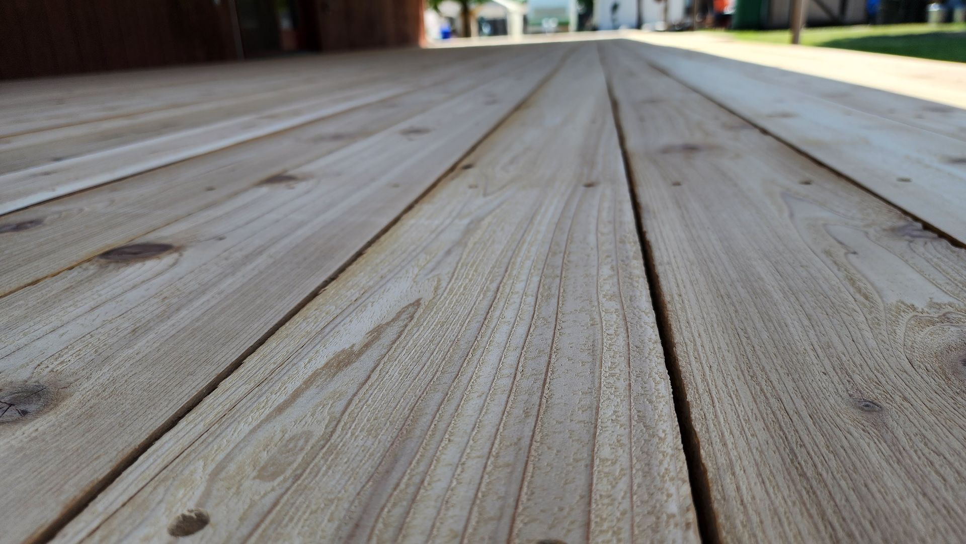 Wooden deck planks, viewed from a low angle, leading toward a blurred outdoor scene.