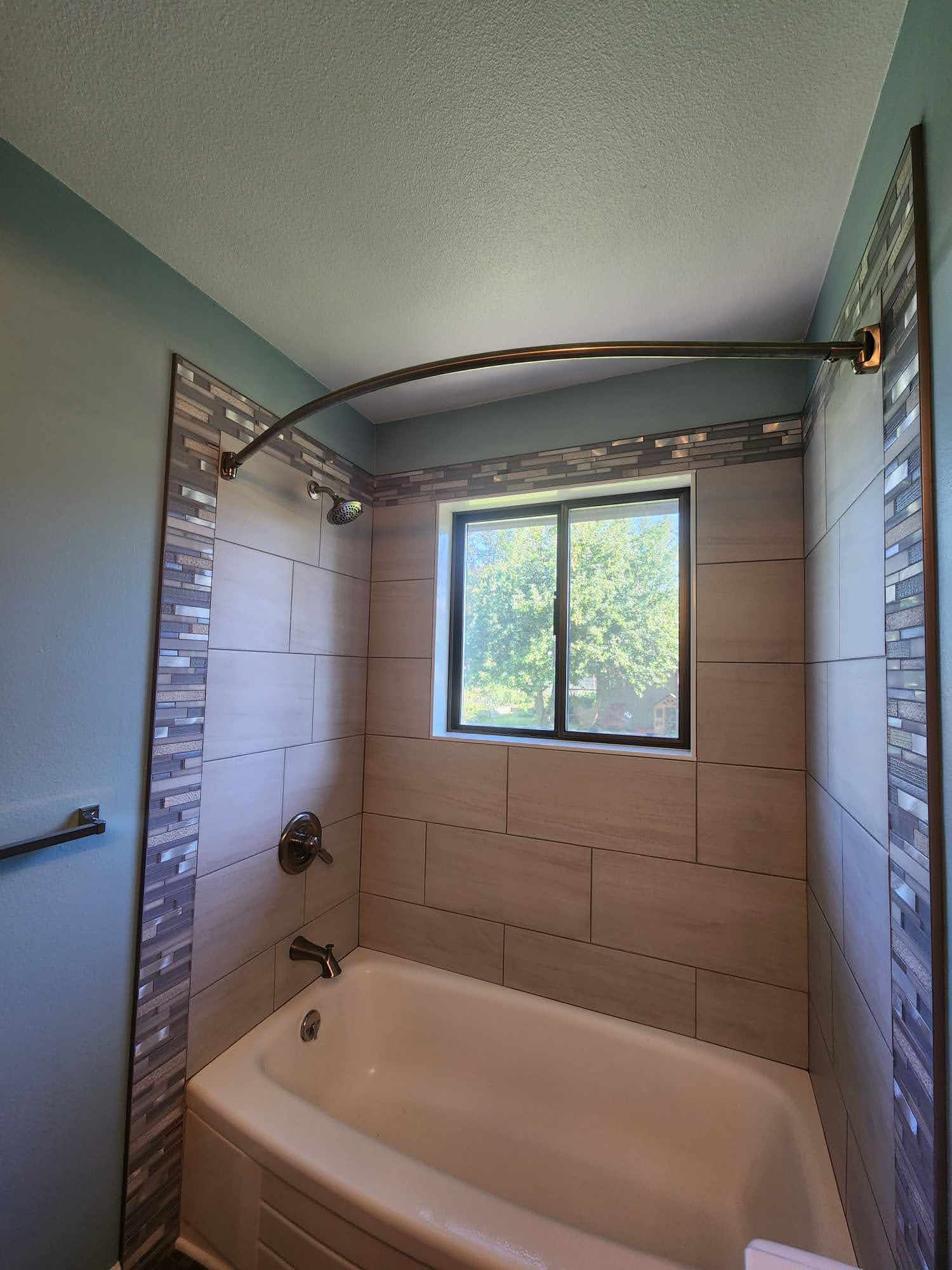 Bathroom with a bathtub, showerhead, and window. Beige tile walls and blue accents.