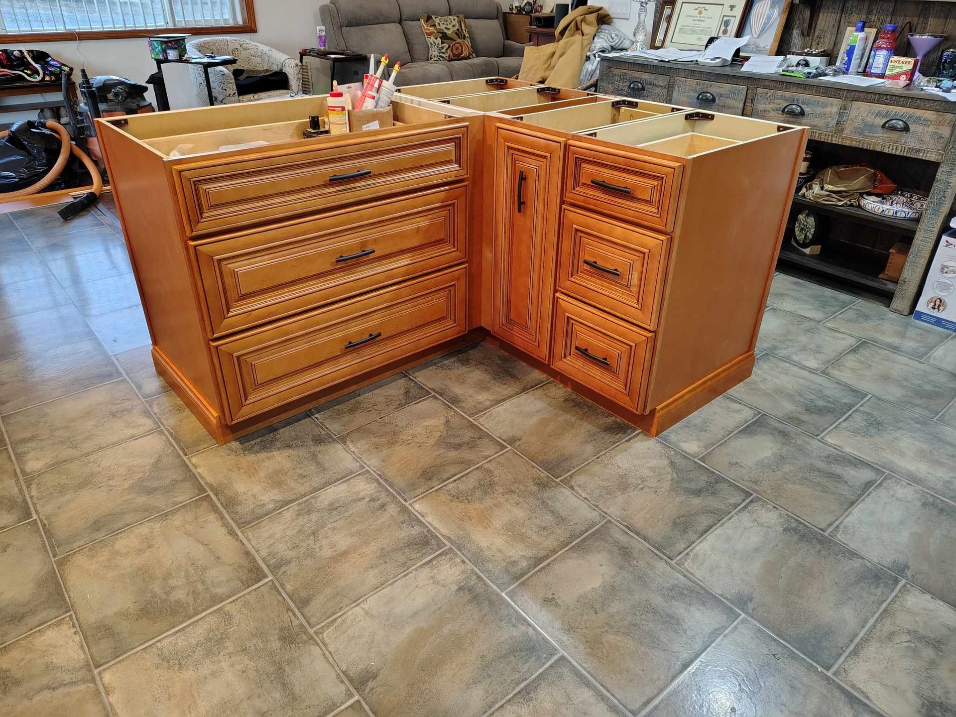 Kitchen cabinets, unfinished wood, L-shaped, on tiled floor.