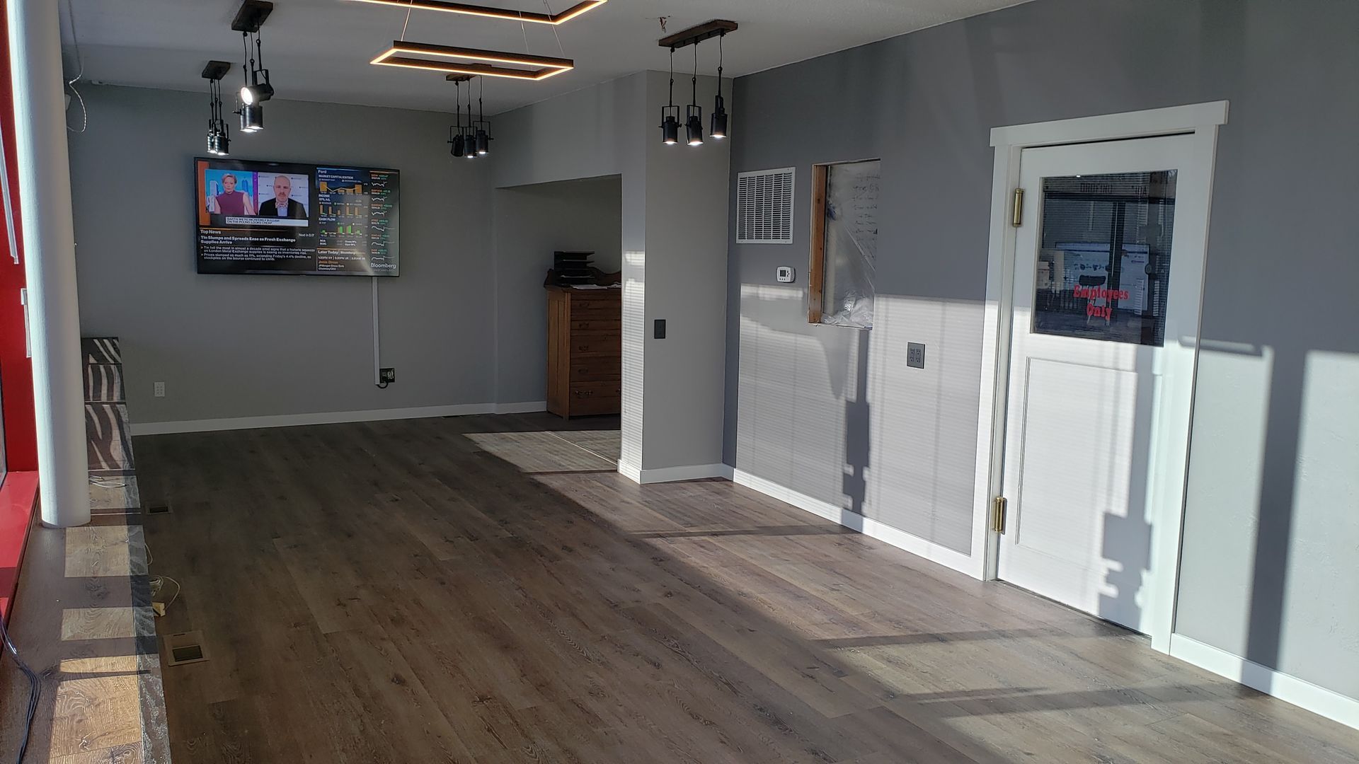 Empty room with gray walls, hardwood floor, white door, and a television.