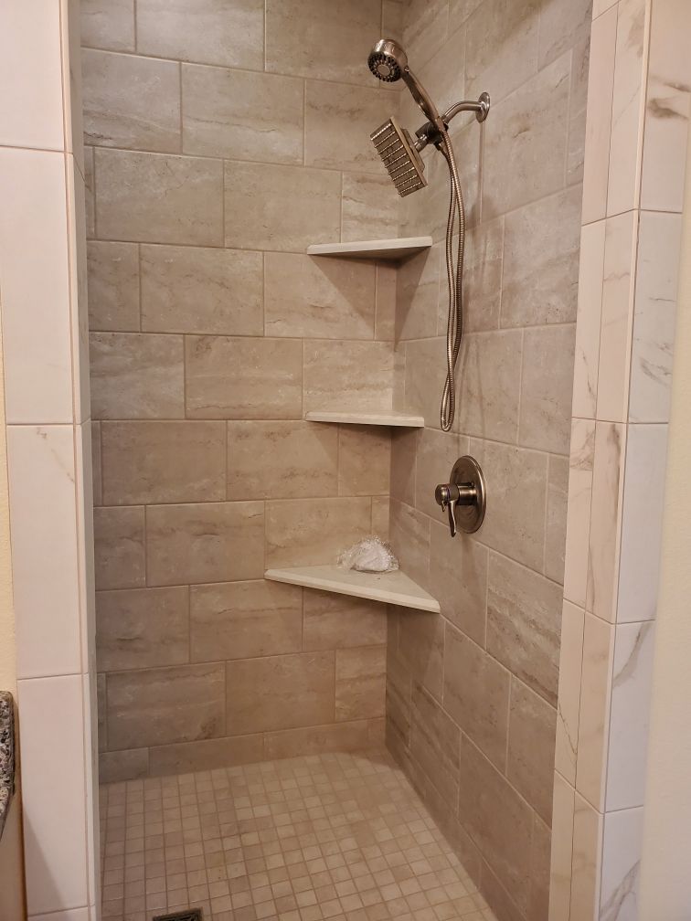 Tiled shower stall with three corner shelves, showerhead, and faucet. Beige tiles and floor.