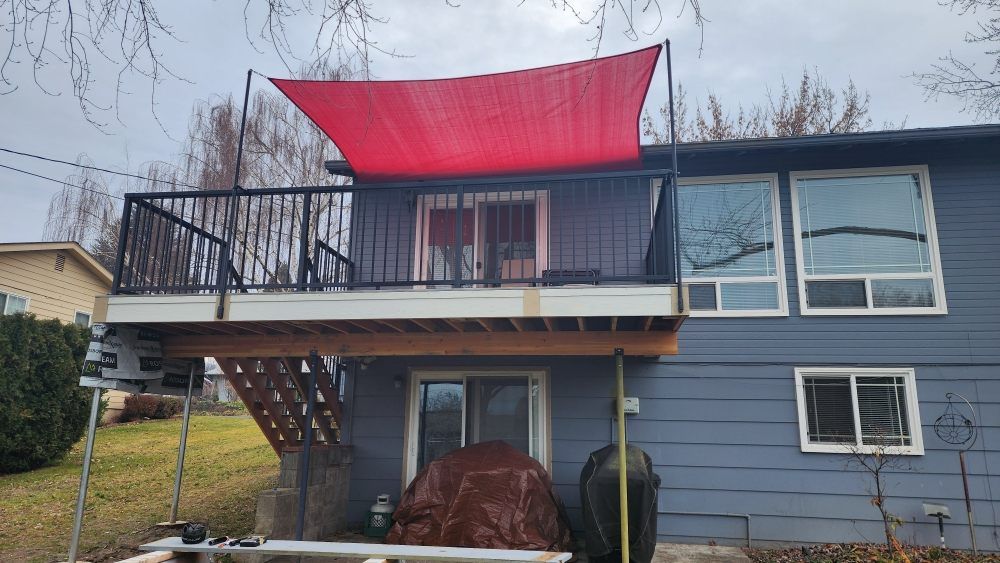 Red sun shade over a black-railed deck attached to a blue house.