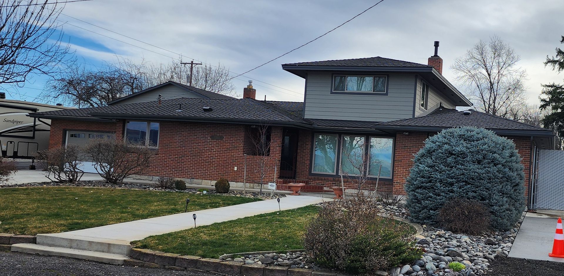 Beige house with gray shingle roof and blue sky.