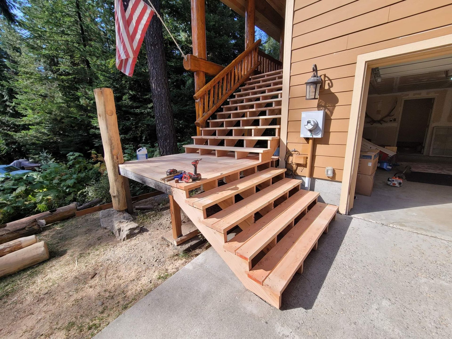 Wooden staircase under construction beside a building with an American flag; the steps have open risers.
