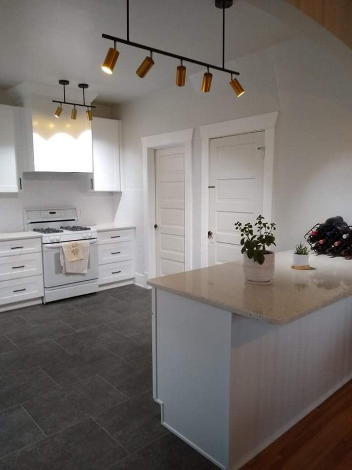 Modern white kitchen with island, white appliances, dark gray tile floor, and track lighting.