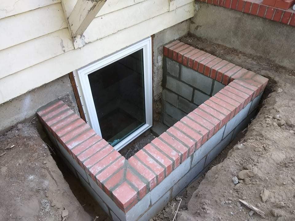 White-framed basement window with a beige corrugated window well. The window is set in a concrete wall.