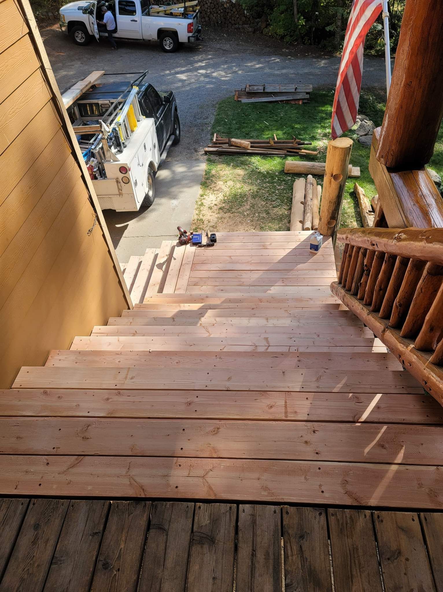 Wooden stairs leading down, with a log railing and a truck in the background.