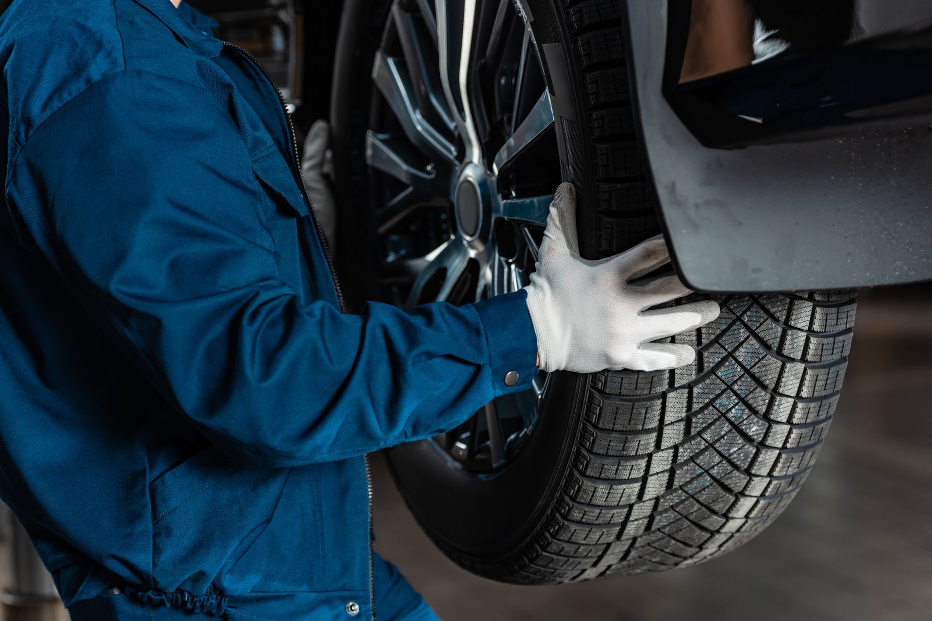 Mechanic in blue coveralls checks a car tire and wheel in a garage