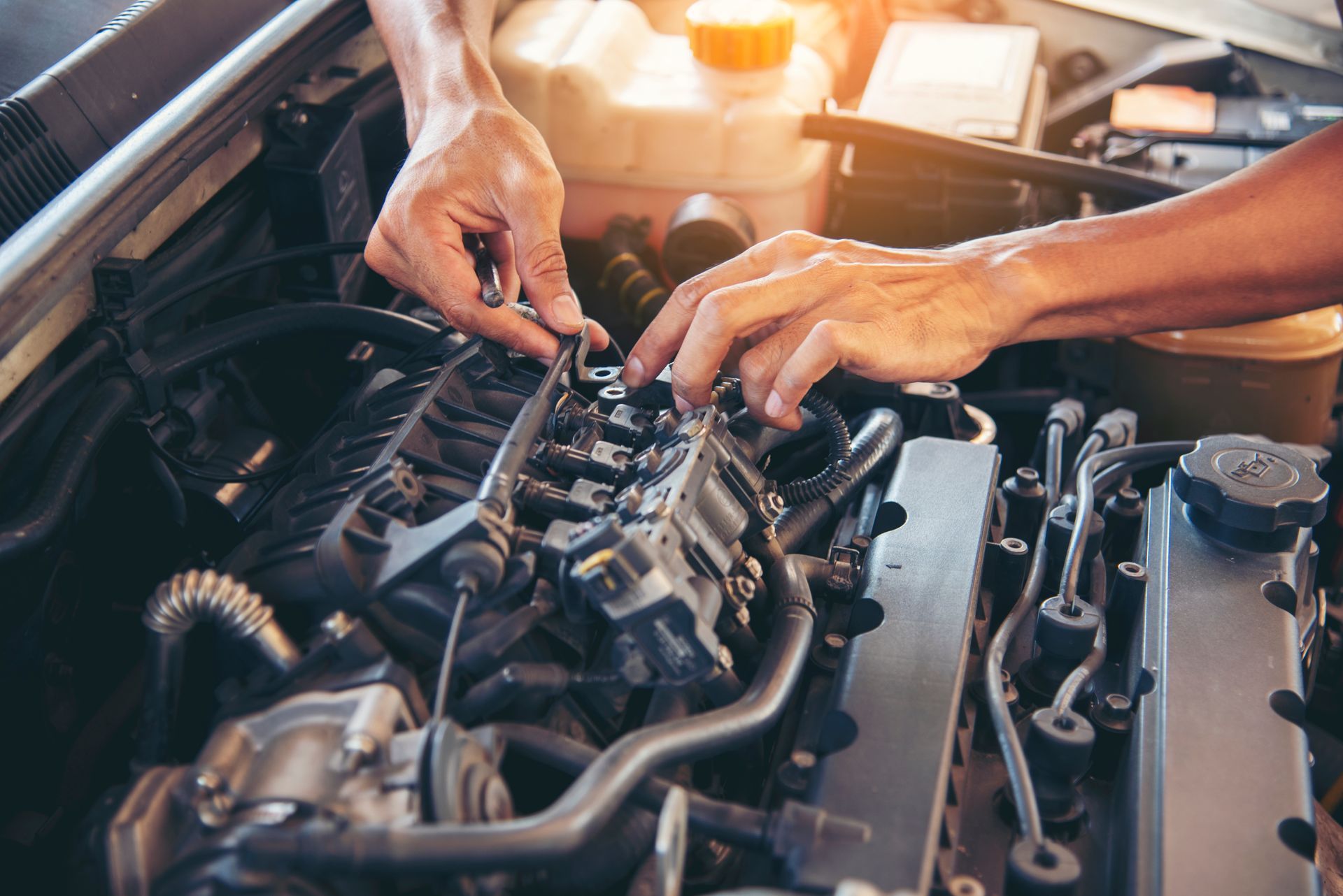 Hands working on a car engine in a garage, with tools and engine components visible