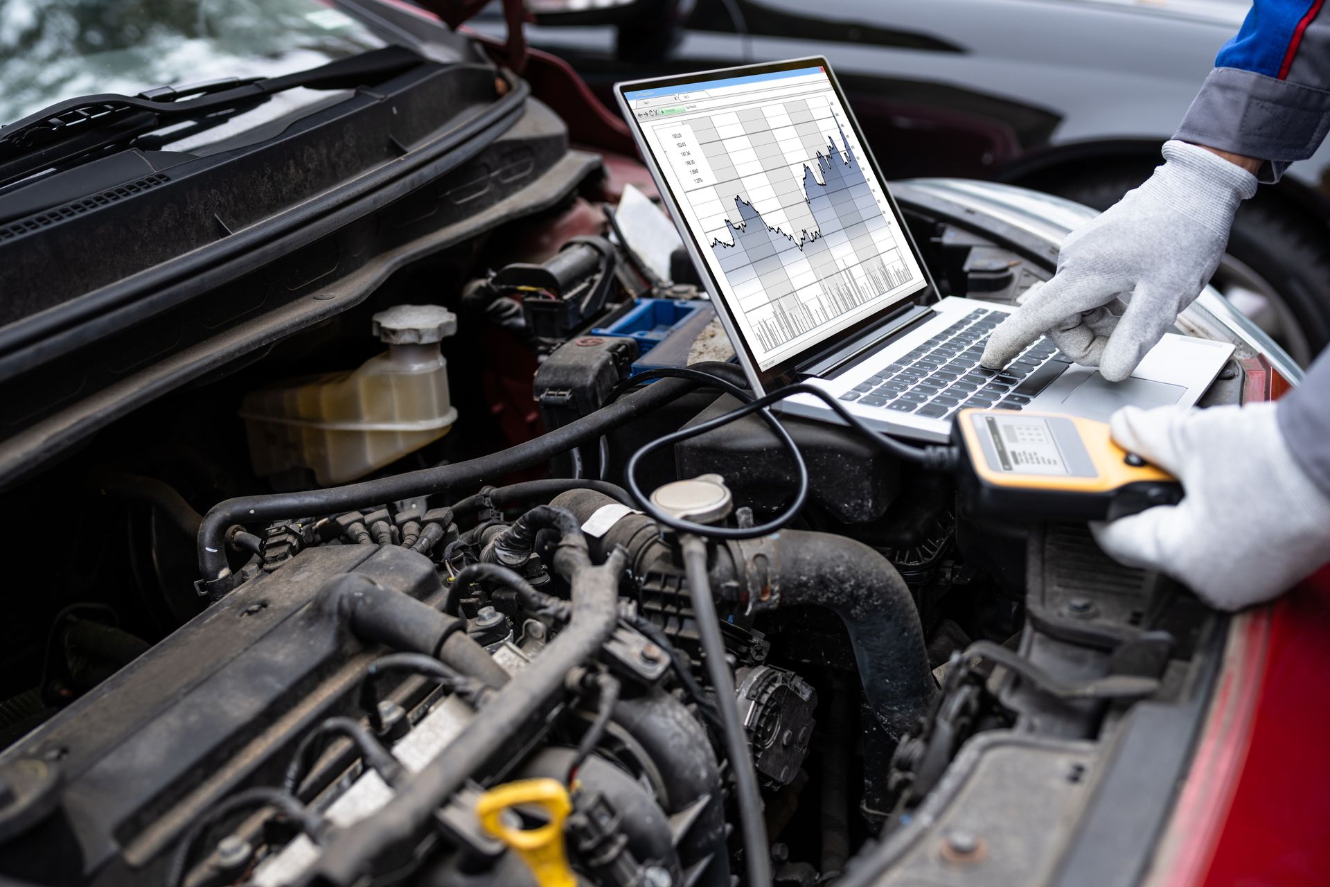 Mechanic using a laptop to diagnose a car engine in an open hood bay