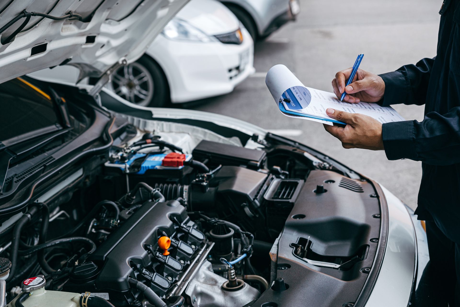Mechanic inspecting a car engine in a garage while holding a checklist and pen