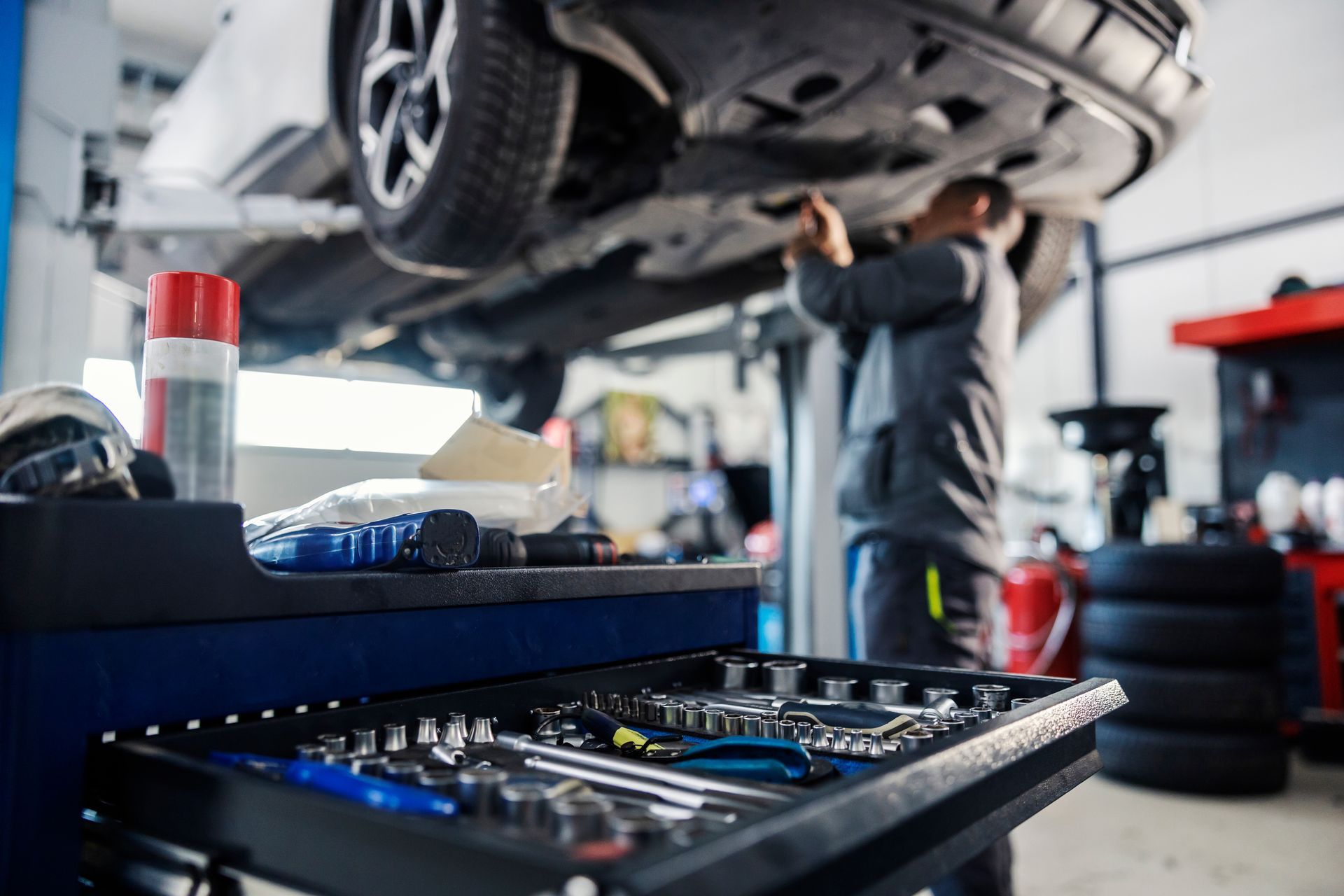 SUVs in a bright auto repair shop with open hoods, lifts, and red tool cabinets