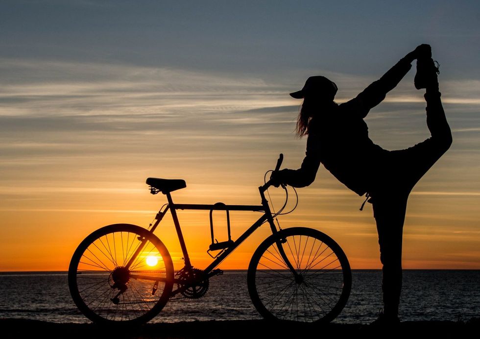 Silhouette of a person doing a yoga pose by a bicycle at sunset on a beach.
