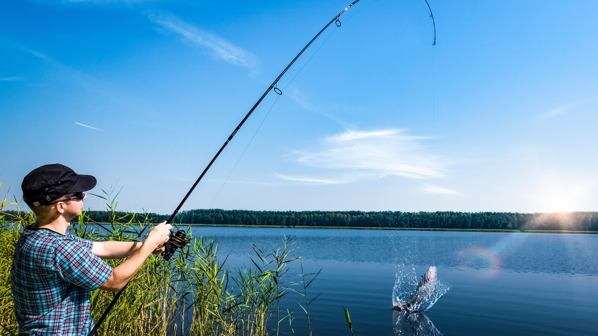Person fishing on a lake, with a fishing rod bent and splashing water. Blue sky and sunlight in the background.