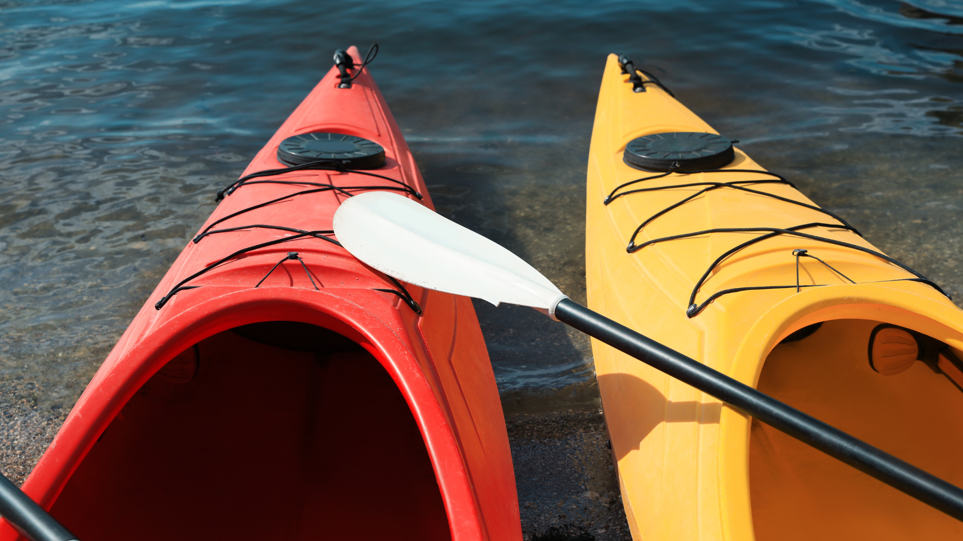 Red and yellow kayaks at water's edge with a paddle resting across them.