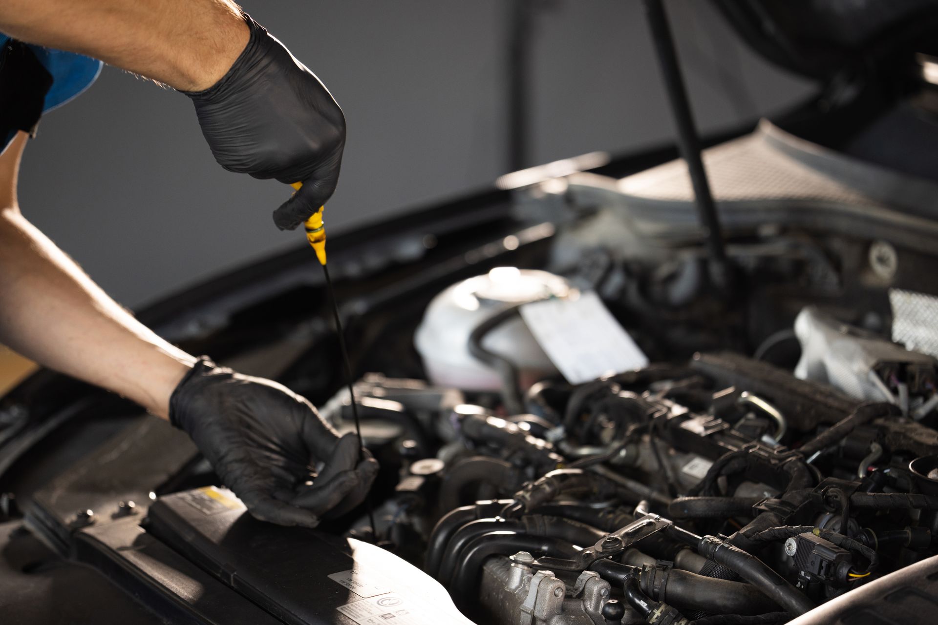 Hands in black gloves checking car oil with a dipstick in engine bay.