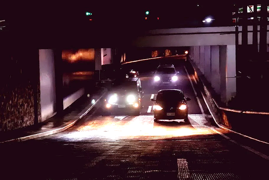 Cars driving into an underpass at night. Headlights illuminate the road ahead.