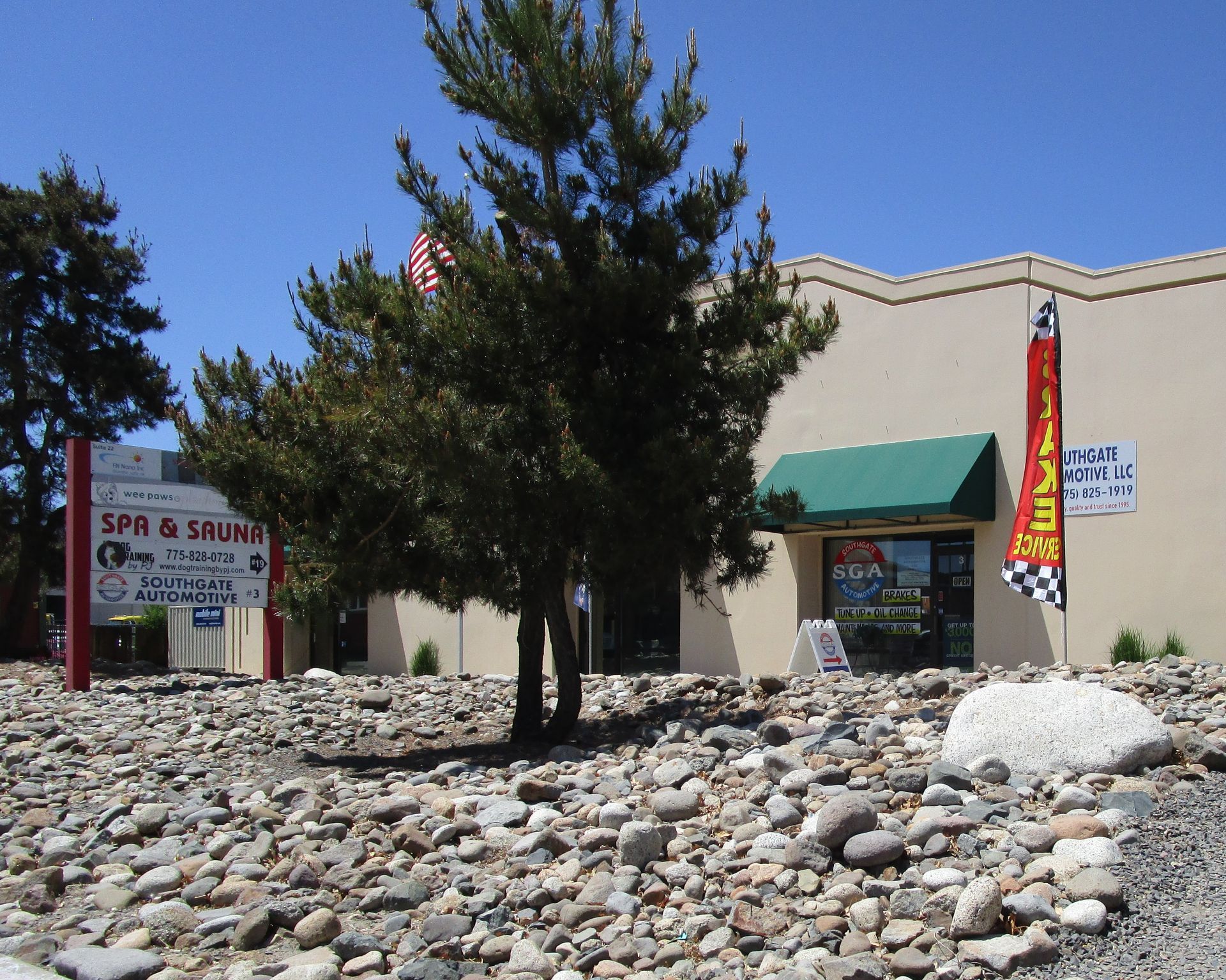 Building with a green awning and sign, tree in front, rocky ground, blue sky.