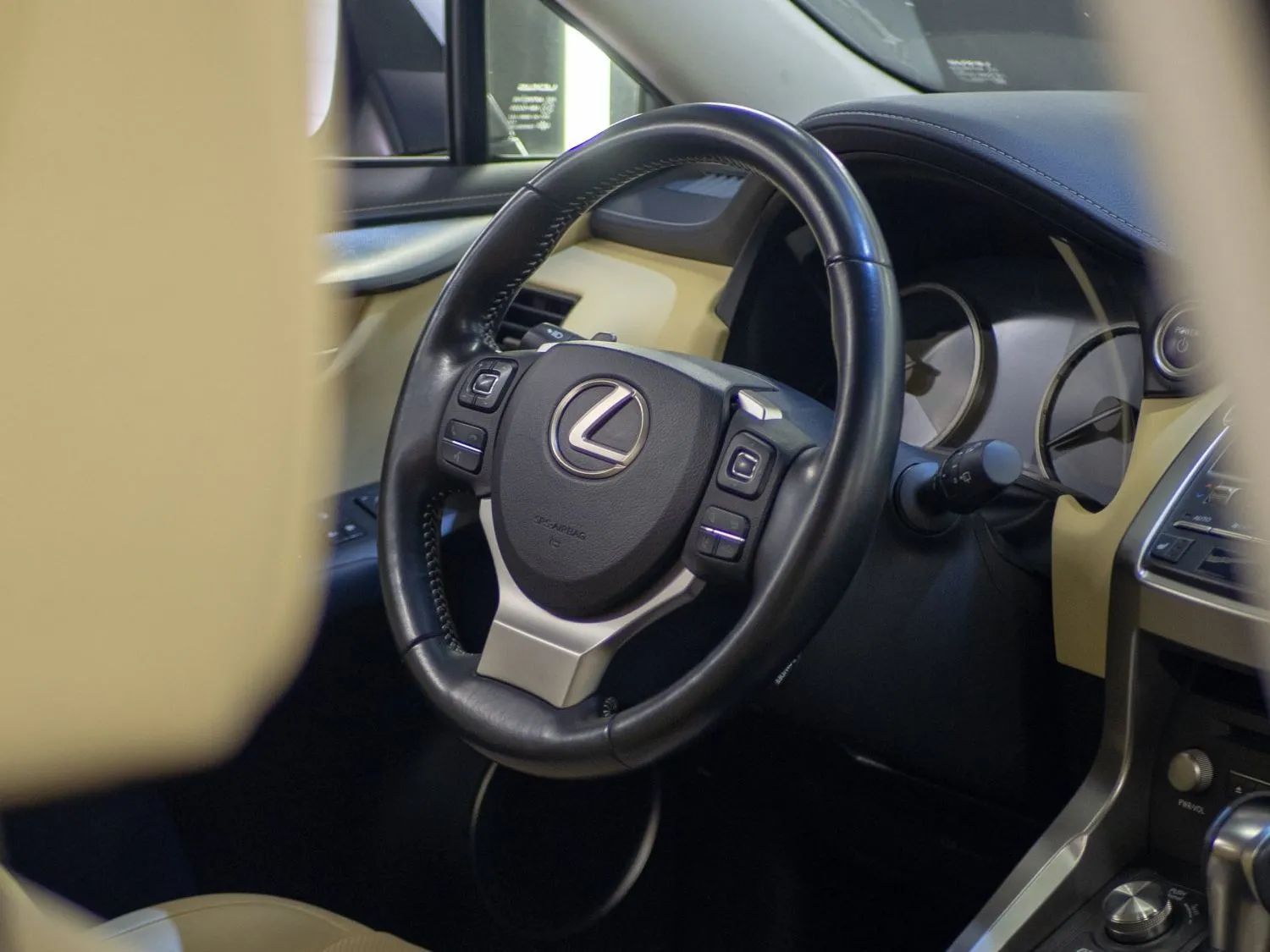 Steering wheel inside a Lexus car, black leather with silver accents, beige interior.