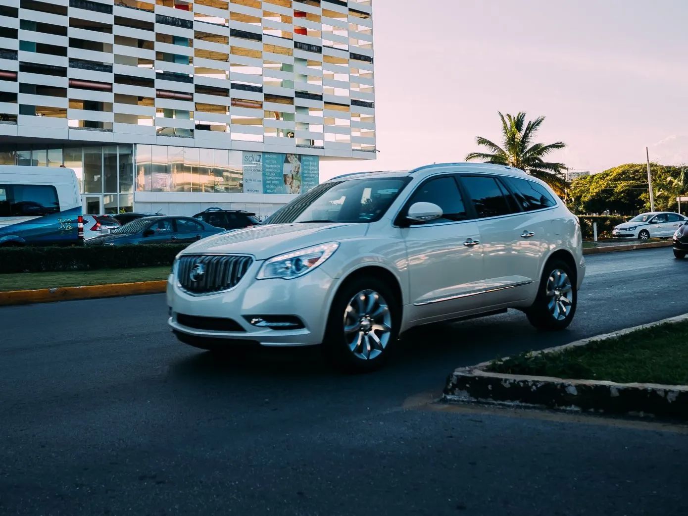 White Buick SUV driving on a road, with a building in the background.