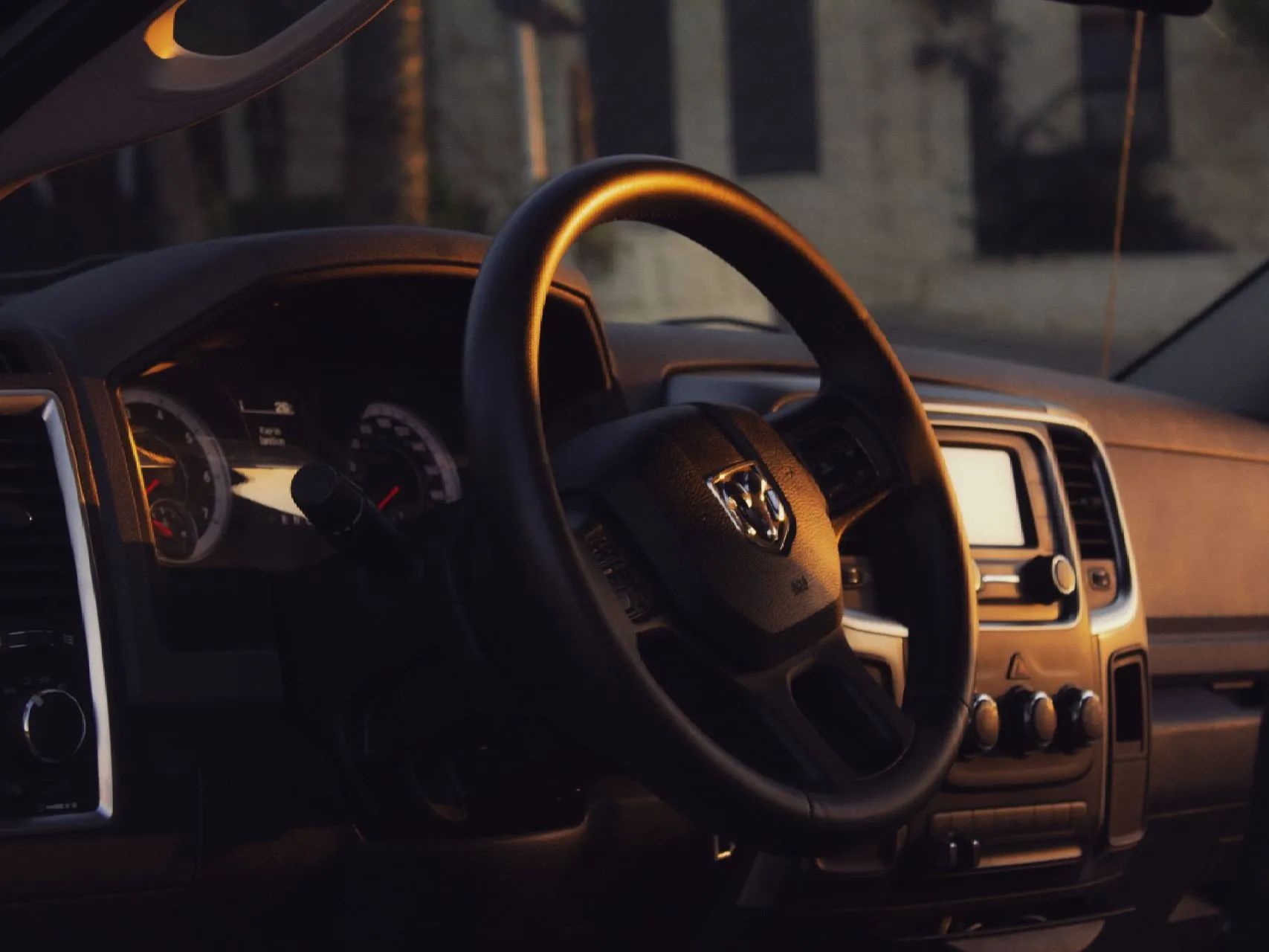 Interior of a Dodge Ram truck, steering wheel in focus, dashboard, gauges, and radio visible, warm lighting.