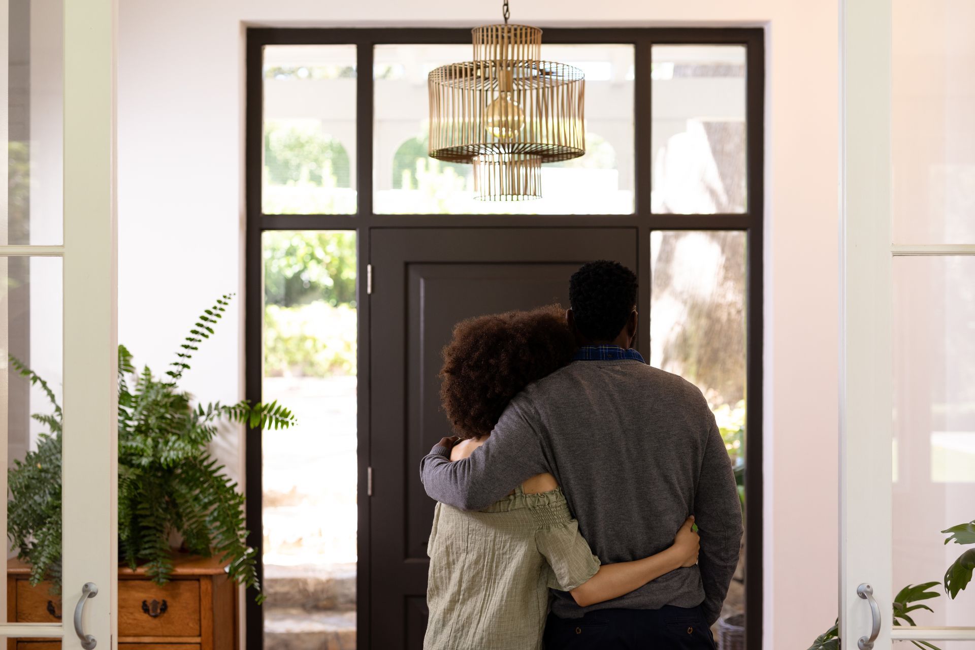 Couple embracing, looking through a front door with a glass panel, likely at their new home.