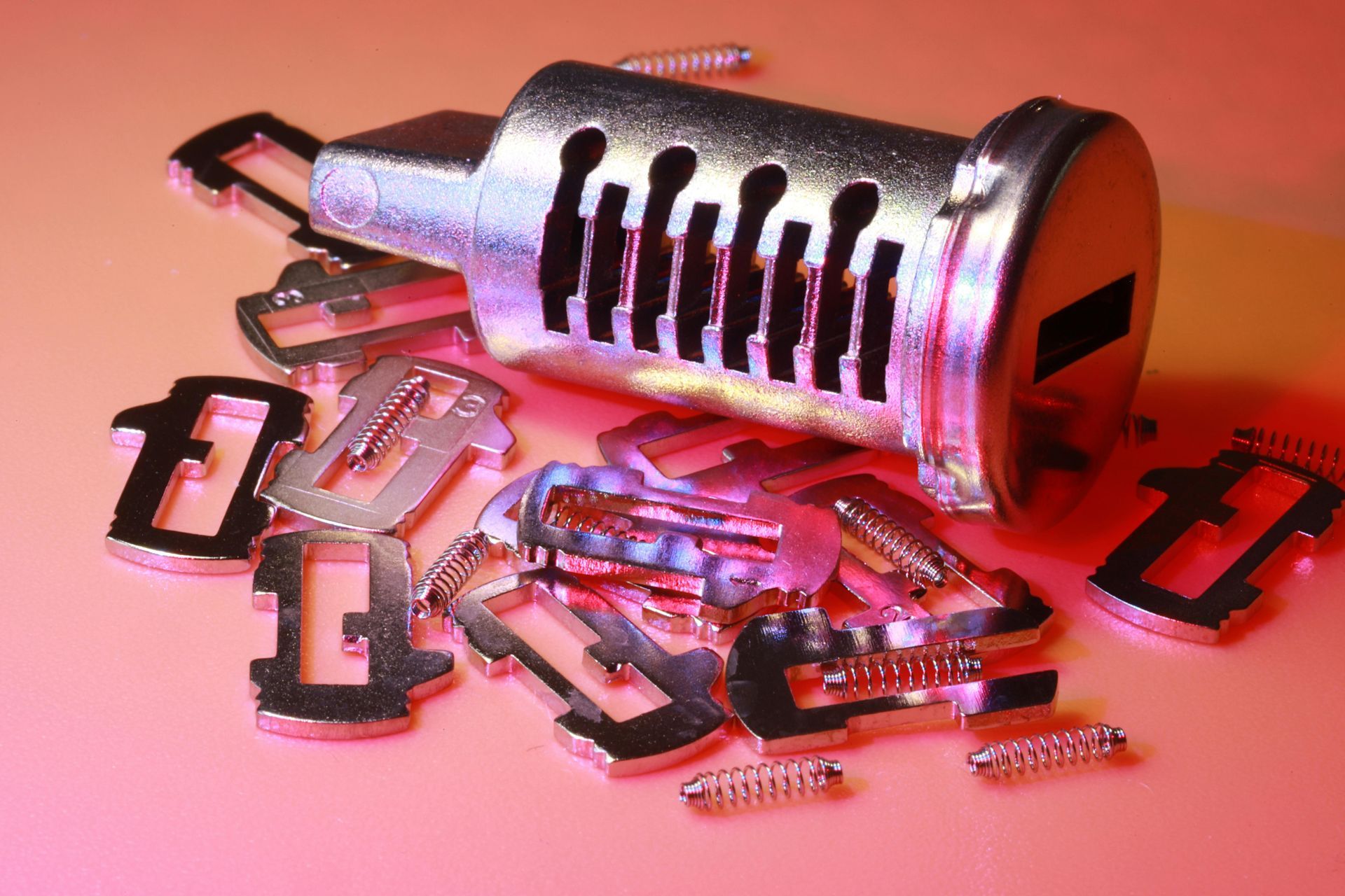Close-up of a disassembled car door lock cylinder with metal wafers and springs scattered on a pink surface.