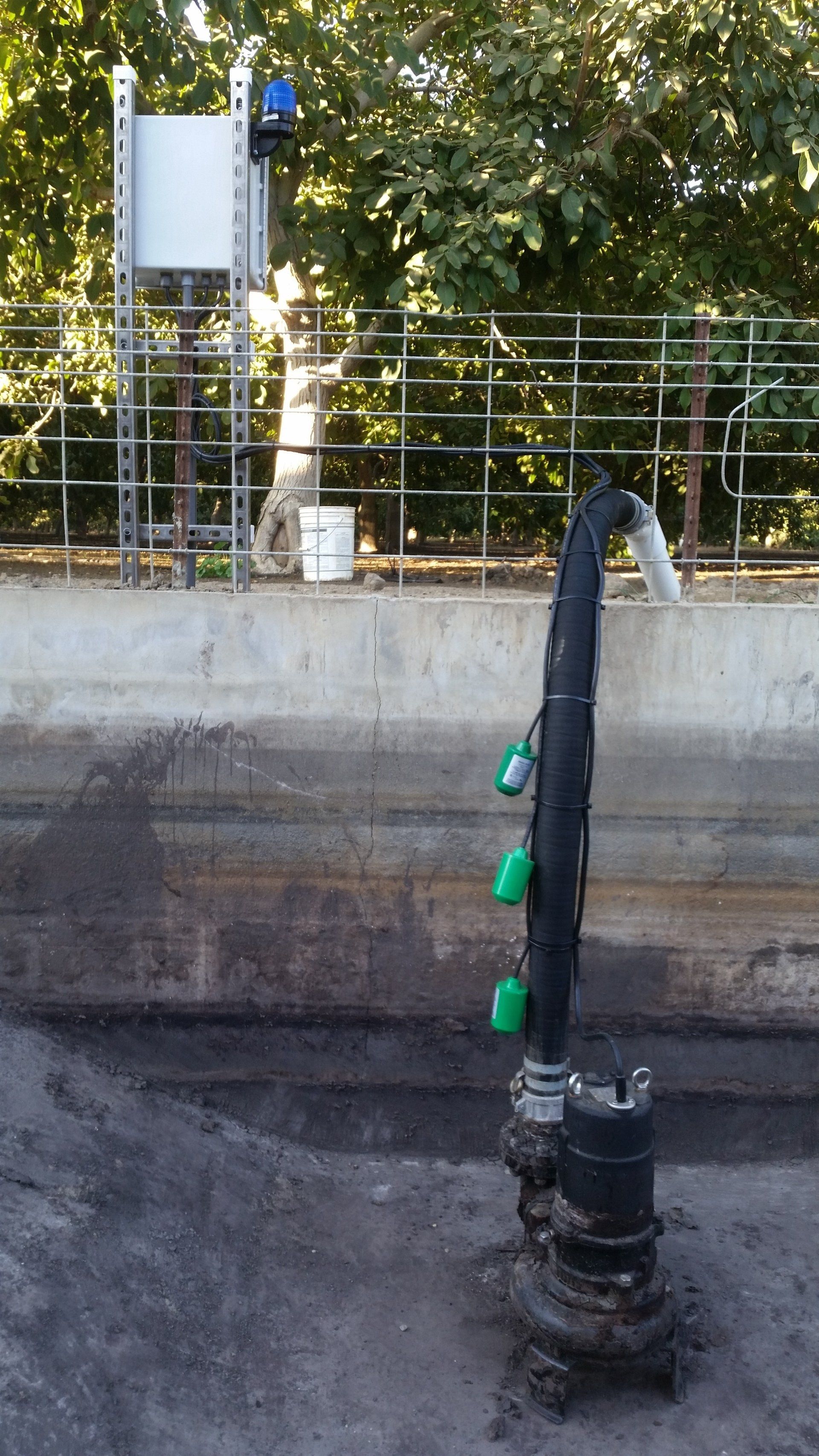 A man is standing on a ladder next to a fence with a hose attached to it.