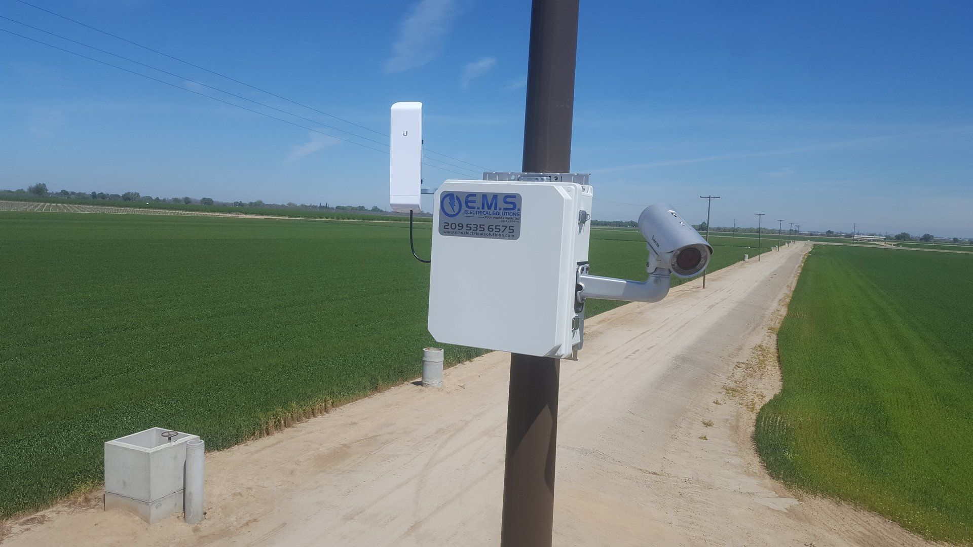 A white box is sitting on a pole next to a dirt road.