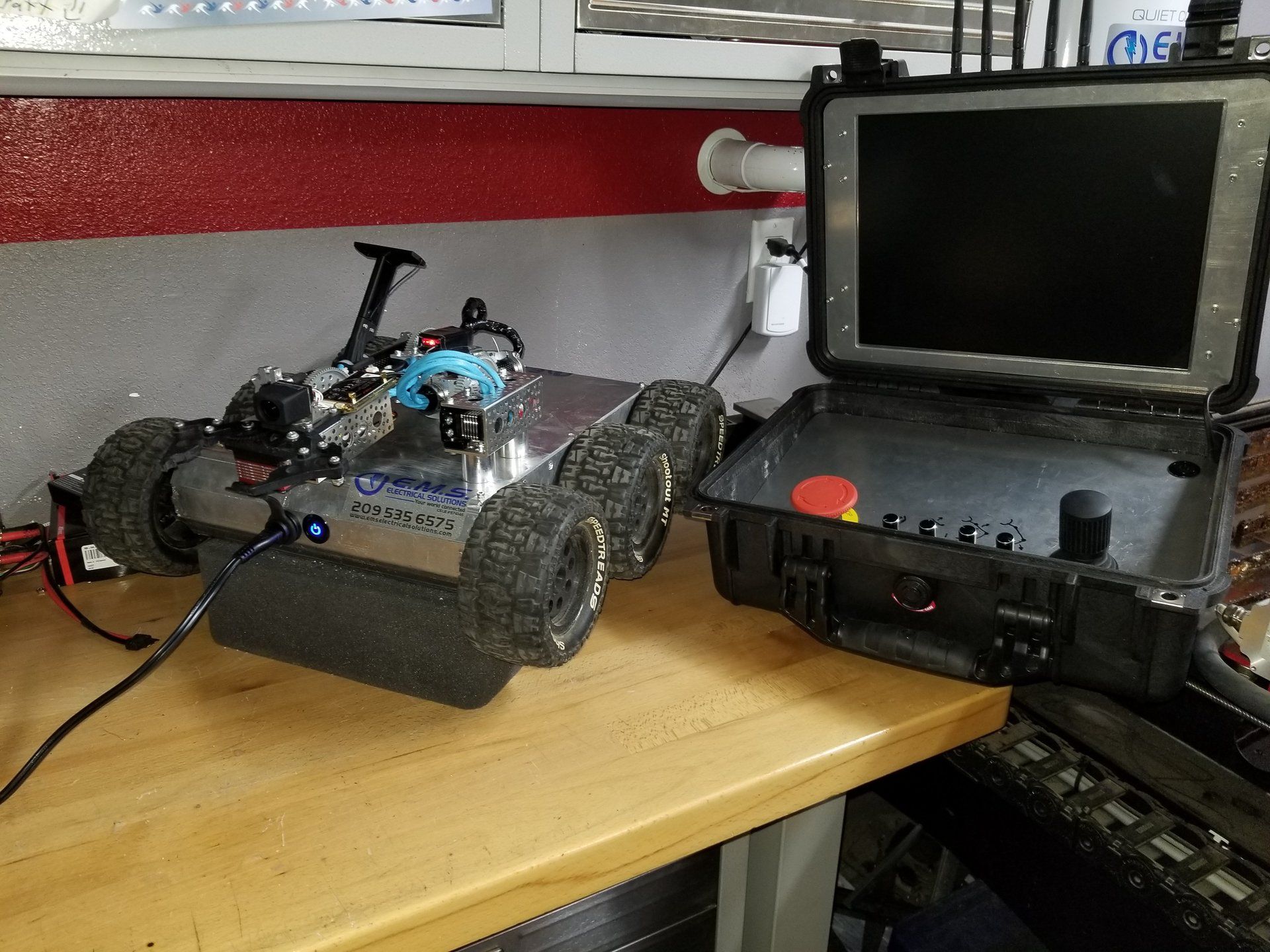 A robot built by e.m.s. is sitting on a wooden table next to a monitor.
