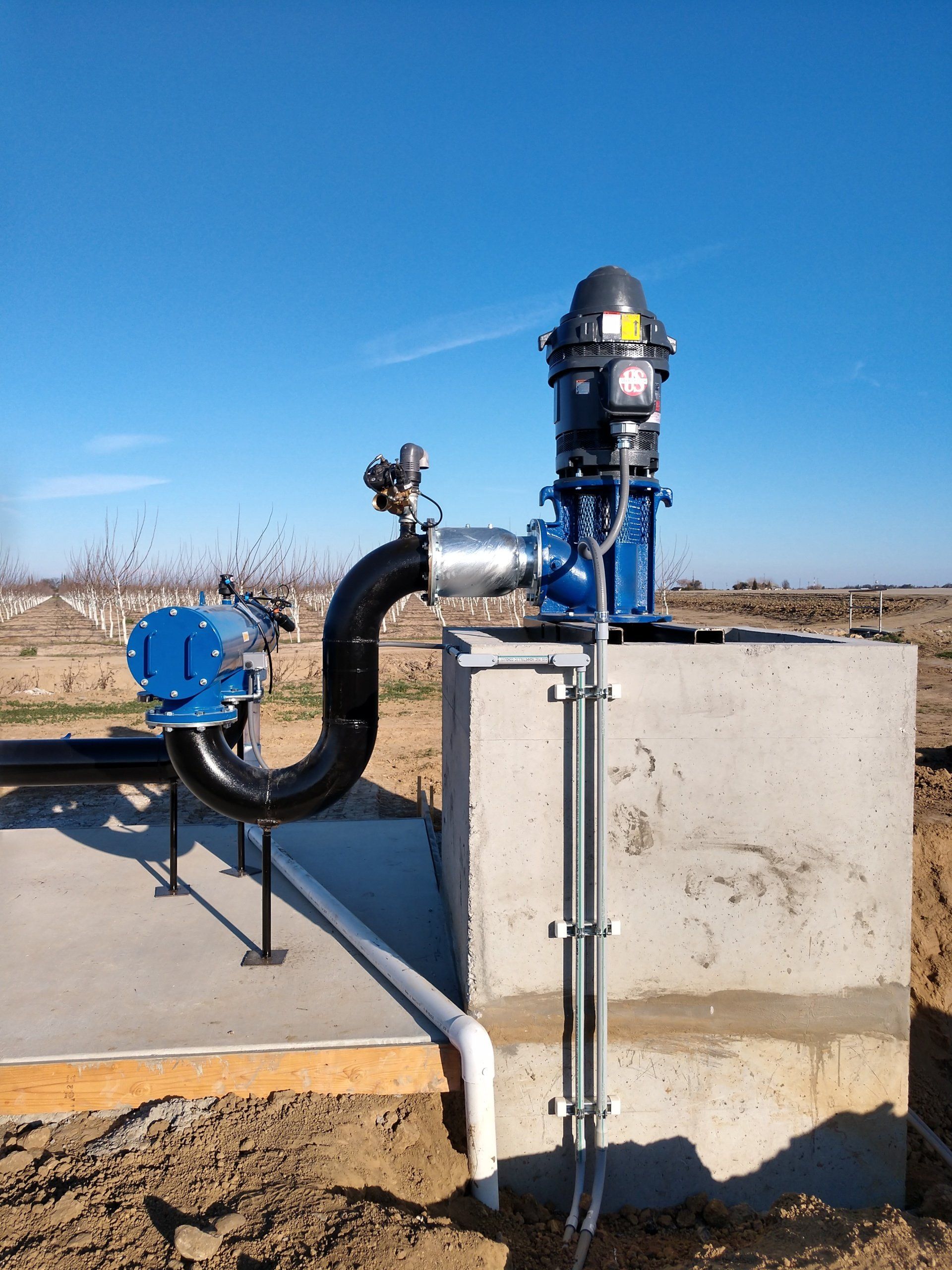 A water pump is sitting on top of a concrete block in the middle of a field.