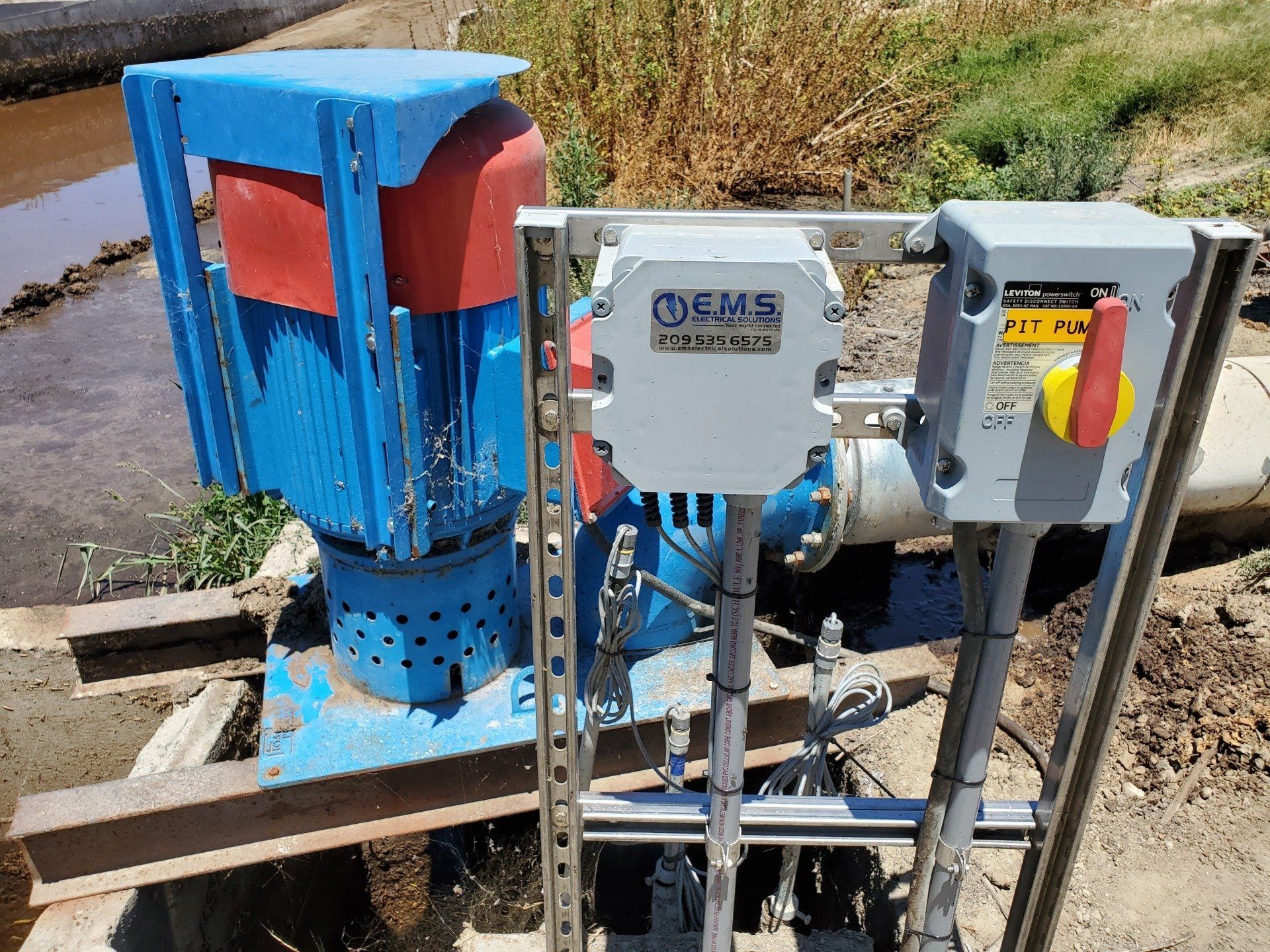 A blue and red water pump is sitting next to a pipe.