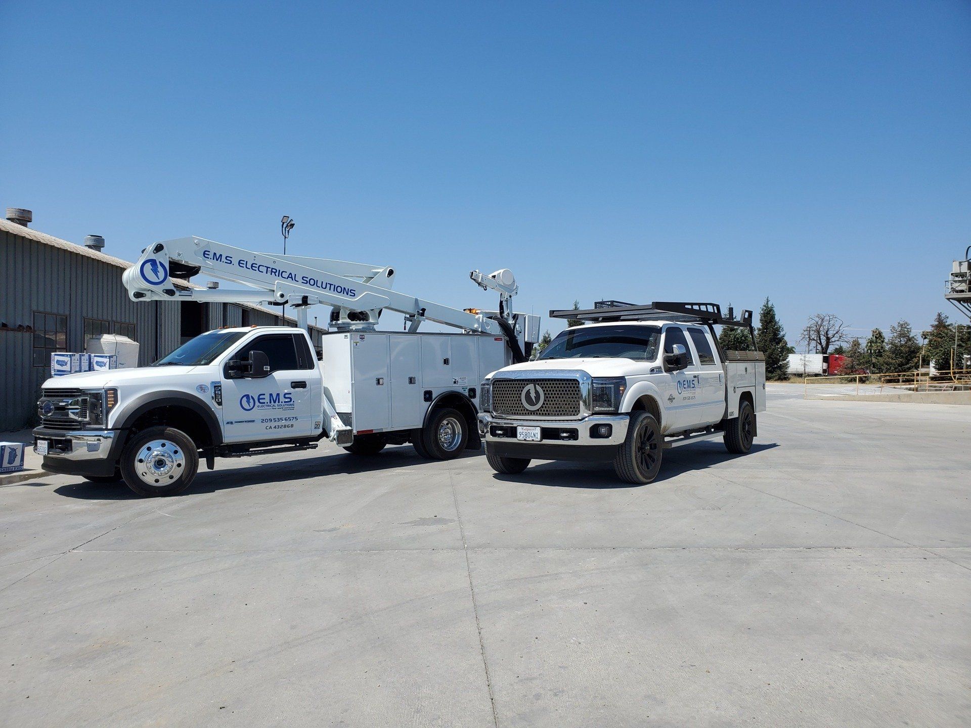 Two EMS Electrical Solutions trucks are parked next to each other in a industrial cement plant