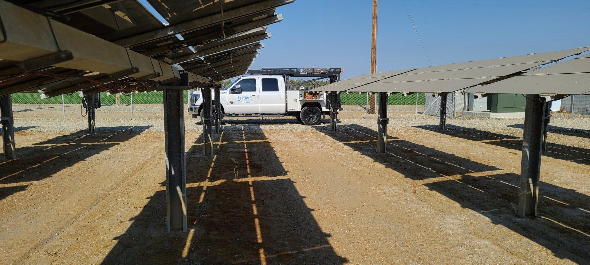 A white EMS Electrical Solutions truck is parked in front of a row of solar panels.