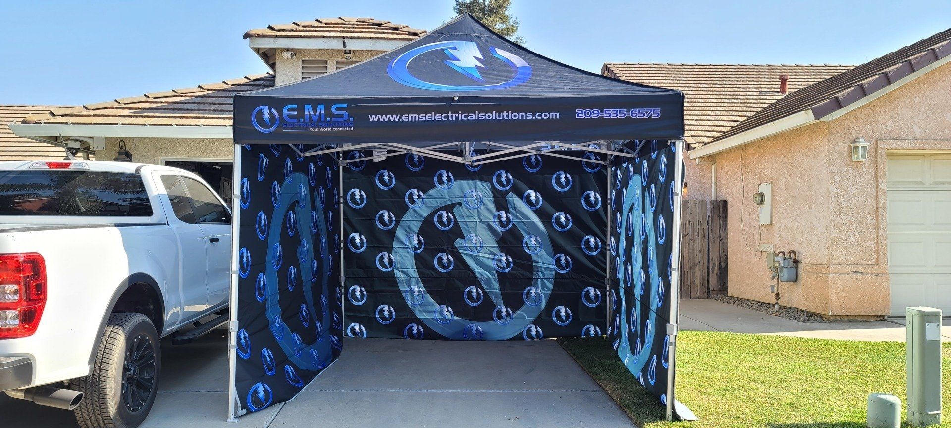A white truck is parked in front of a canopy in a driveway.