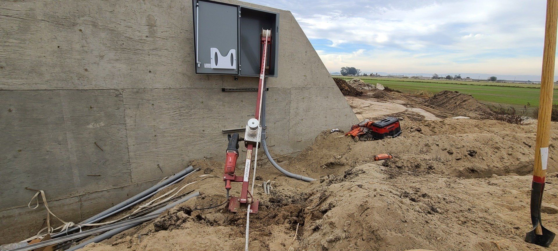 Eine Kiste mit dem Buchstaben M darauf steht neben einer Schaufel im Dreck.