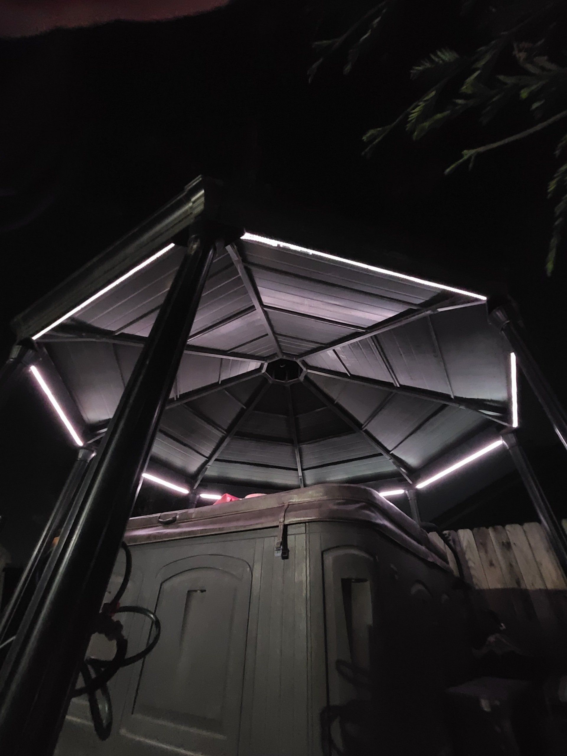 Un gazebo con una vasca idromassaggio sottostante è illuminato di notte.