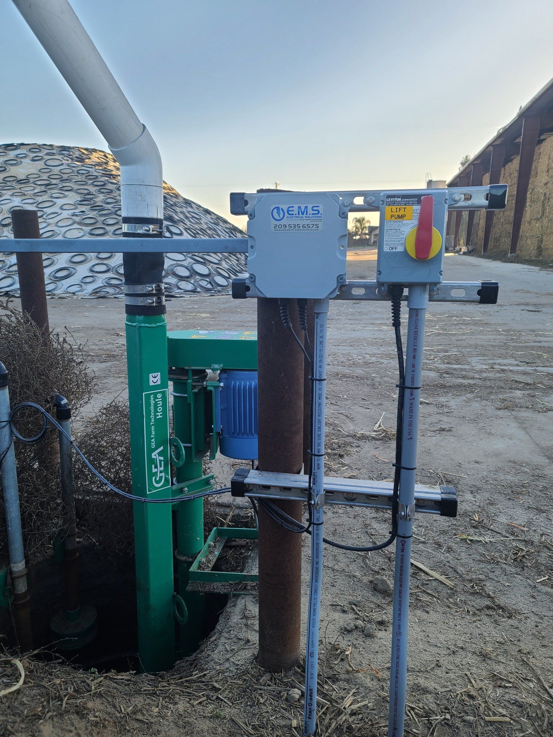 A green pump is sitting in the dirt next to a pole.