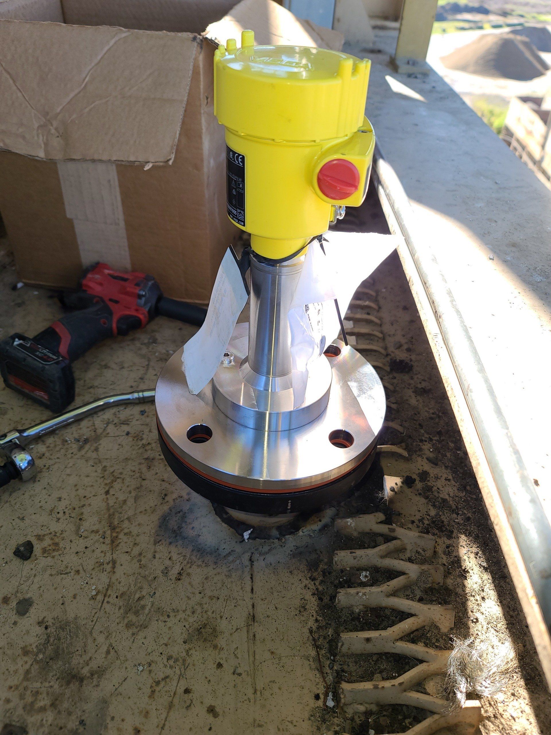 Un dispositivo giallo è appoggiato su un tavolo accanto a una scatola e a un trapano.