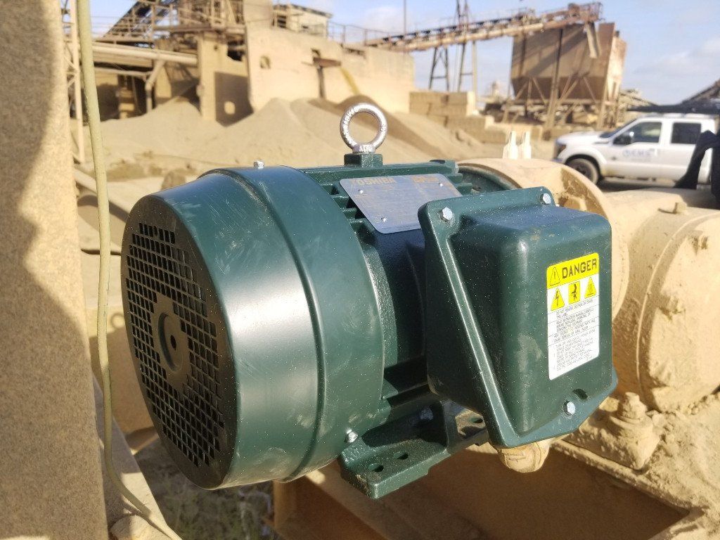 A green electric motor is sitting on top of a sandy surface.