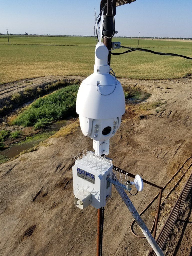 An aerial view of a security camera hanging from a pole in a field.