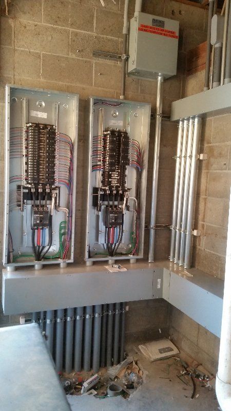 There are two electrical panels in a room with a brick wall.