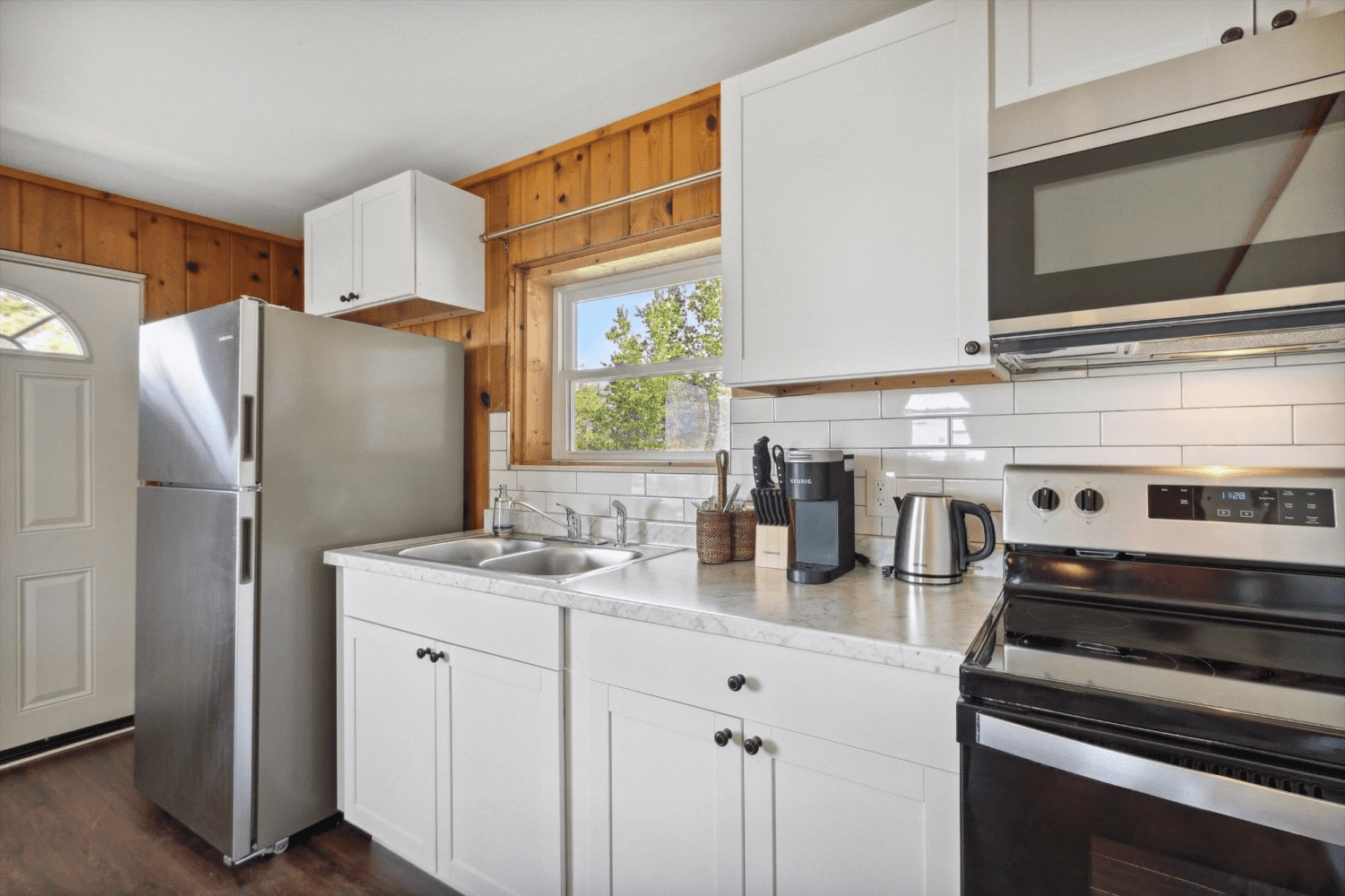 A kitchen with white cabinets , stainless steel appliances , a refrigerator , stove and microwave.