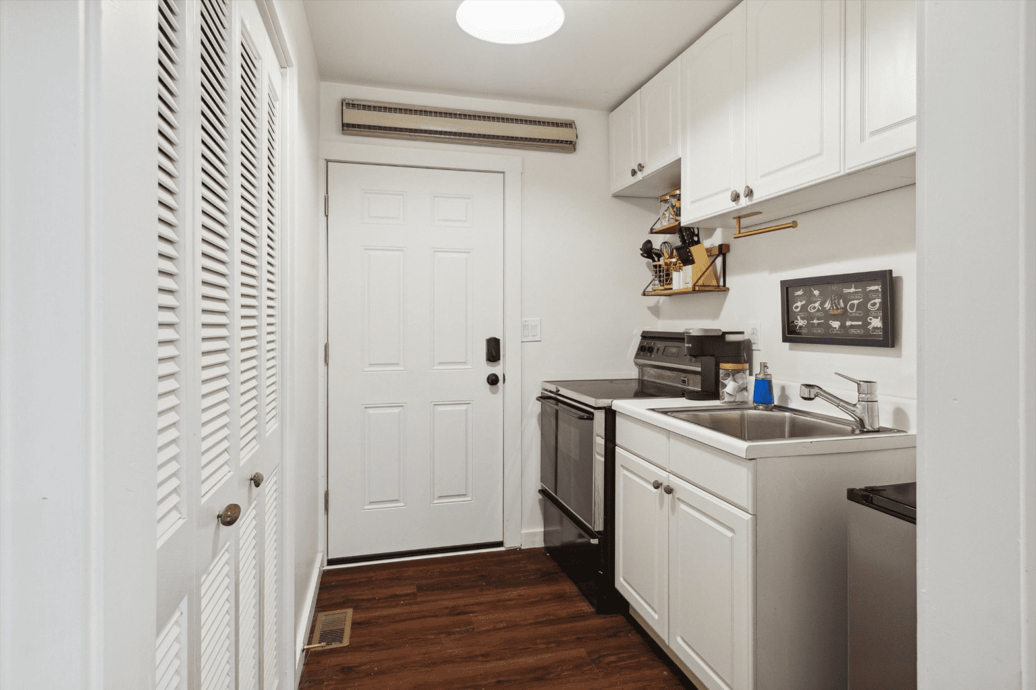 A kitchen with white cabinets , a sink , a stove , and a door.