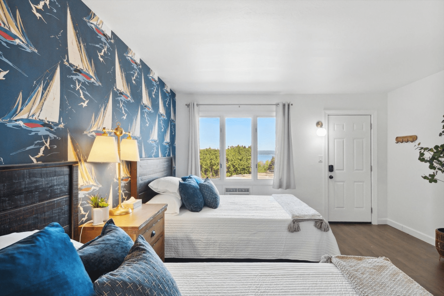 A bedroom with two beds , a window and a sailboat wallpaper.