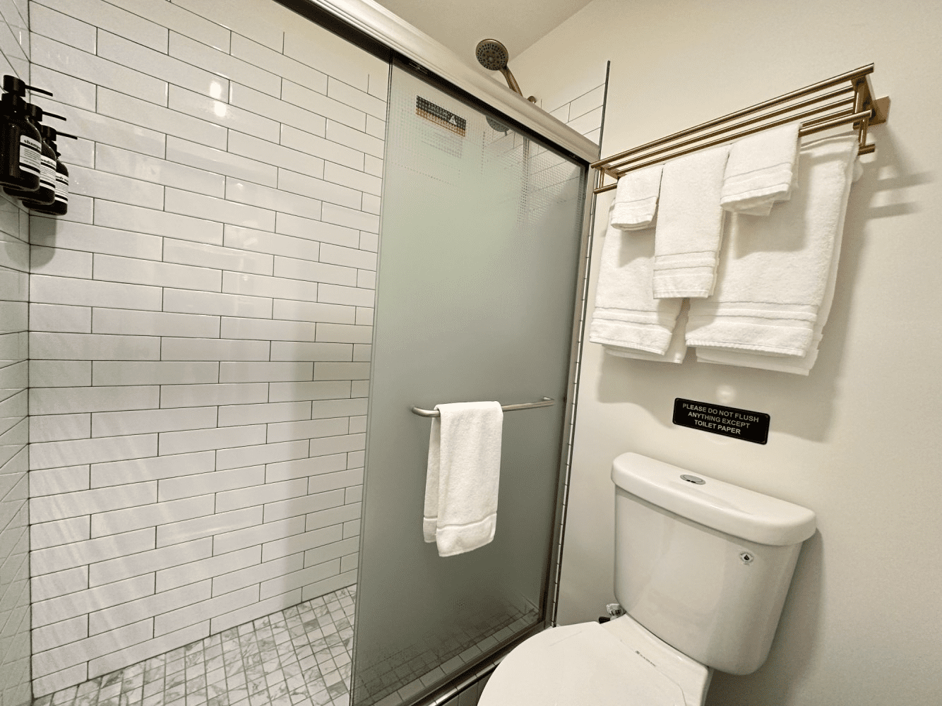 A bathroom with a toilet , shower , and towels hanging on the wall.